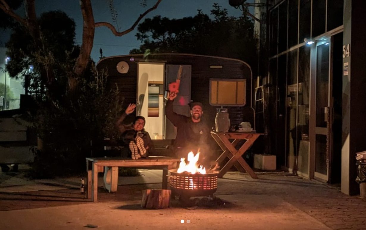 The Kata founders by the campfire beside a vintage caravan at dusk