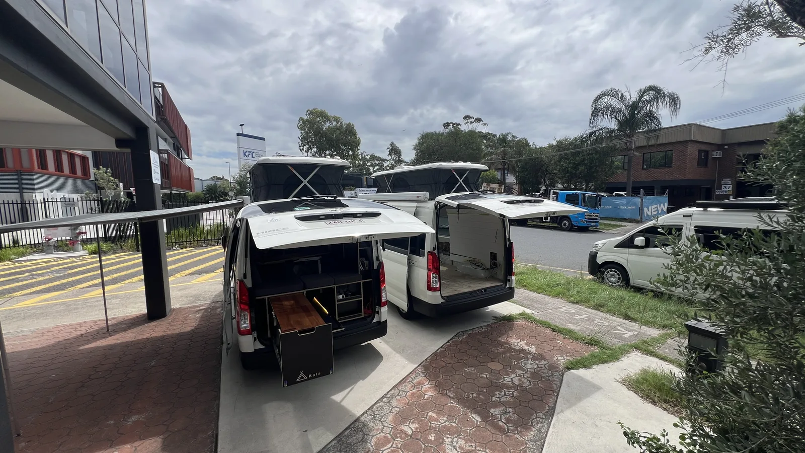 Two HiAce vans mid-build with roofs raised at the Kata workshop